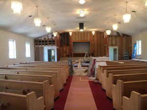 A church interior featuring pews and a partially renovated ceiling, showcasing construction materials and scaffolding.