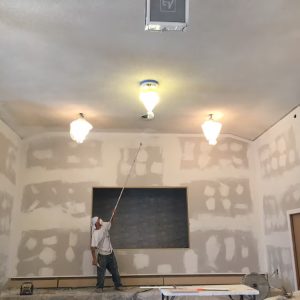 A man is painting the ceiling of a room, focused on his task with a brush and ladder.