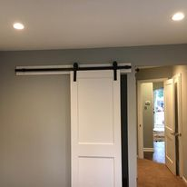 A rustic barn door stands in a room beside a sleek white door, blending traditional and modern design elements.